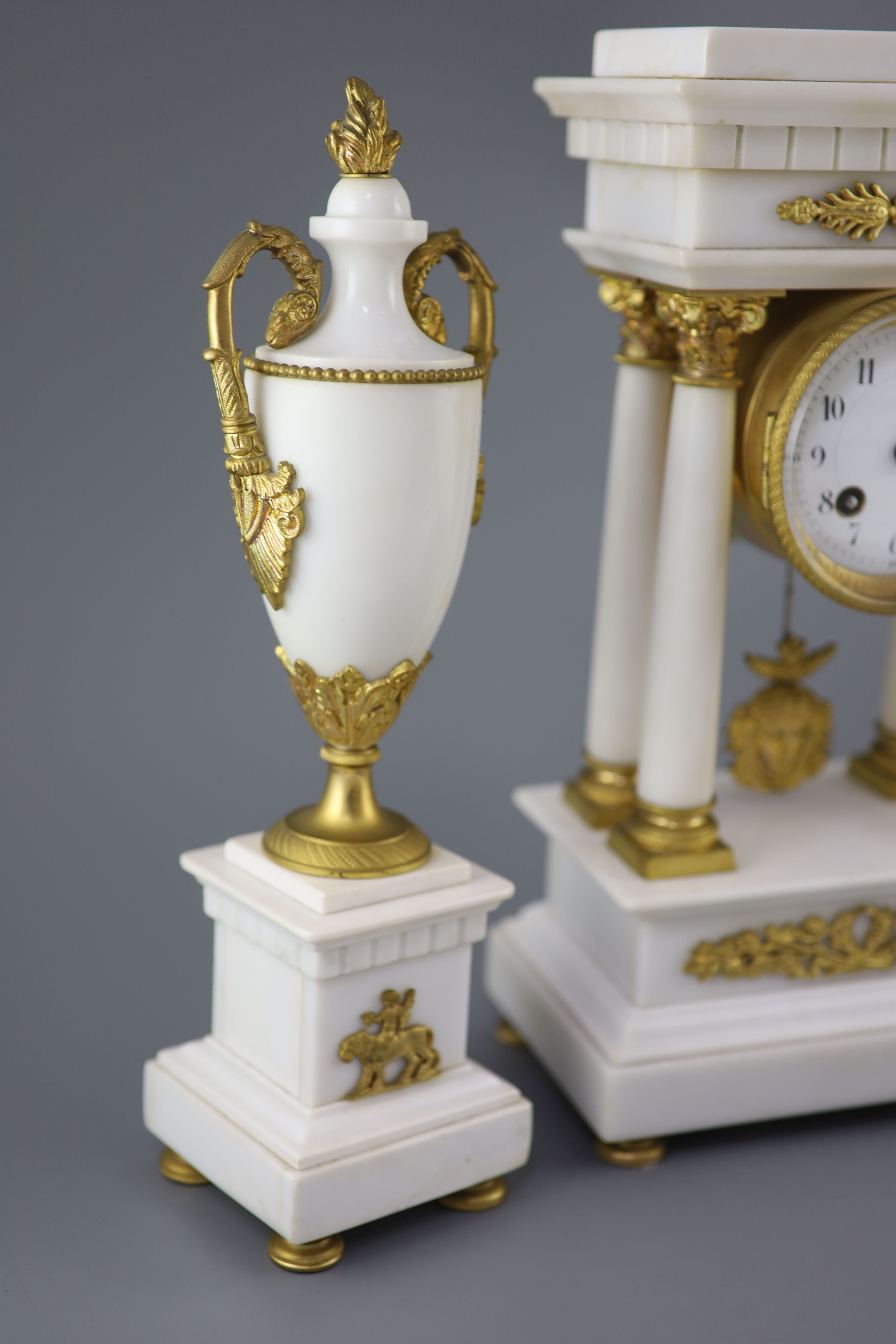 A Louis XVI style ormolu mounted white marble clock garniture, clock 14.5in. urns 13.75in.